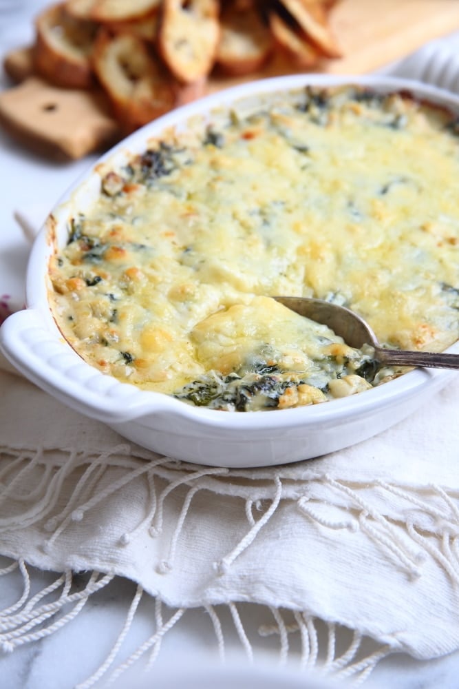 Warm spinach and artichoke dip in a baking dish with a spoon. 