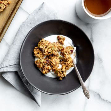 A bowl of granola clusters in a bowl over yogurt with a cup of tea alongside.