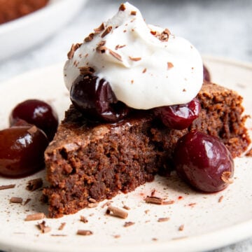 almond flour chocolate cake on a plate with whipped cream and cherries