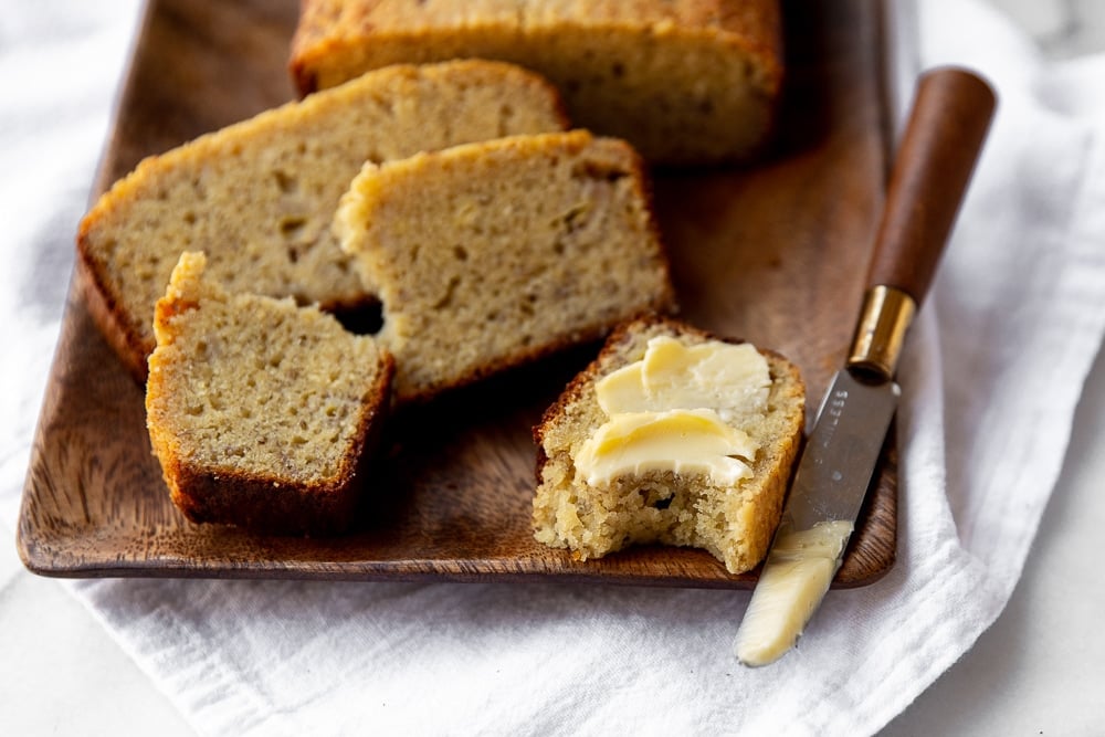 Gluten free banana bread slices on board with butter knife and butter