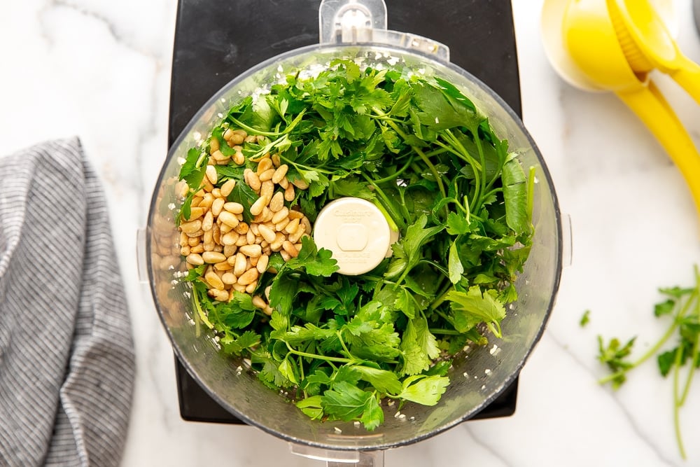 Process shot showing herbs, garlic and pine nuts in food processor