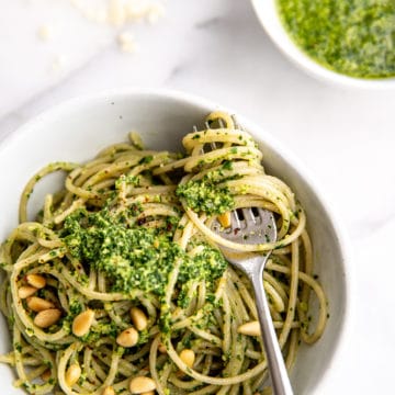 Spaghetti in bowl topped with green sauce, with fork