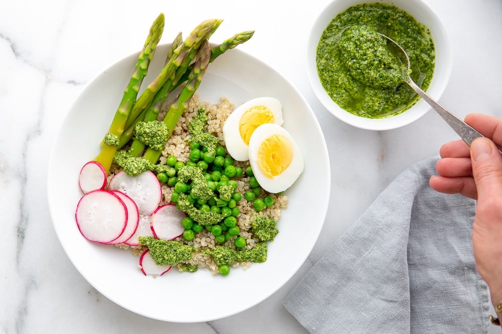 Green sauce drizzled over grain bowl with asparagus and peas