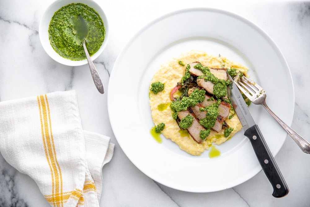green sauce drizzled over polenta and pork on plate