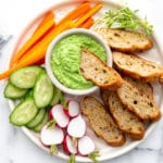 Creamy pea dip in bowl with platter of vegetables and crostini for dipping