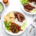 Steak burrito bowls with skirt steak, vegetables, romaine lettuce, tortilla chips and avocado crema sauce over rice.