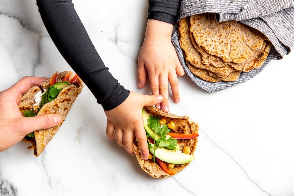 Hands on the counter grabbing tacos made with cassava tortillas.