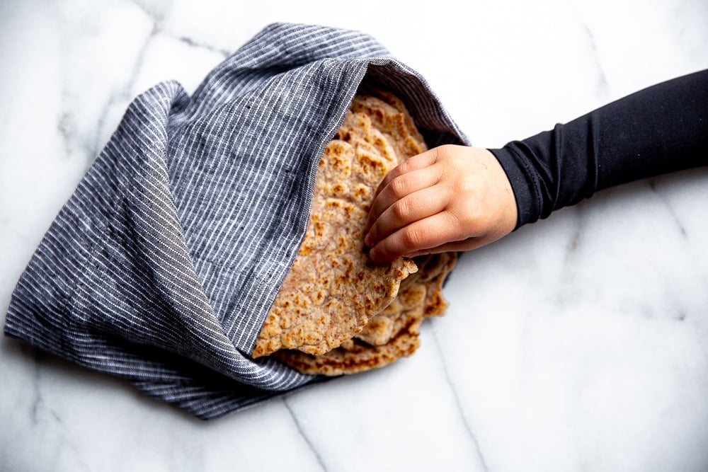 Cassava tortillas wrapped in a towel with a hand pulling one out.