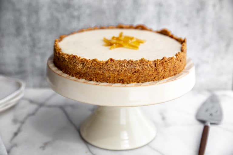 Creamy lemon pie with almond crust on cake stand with pie server on the side