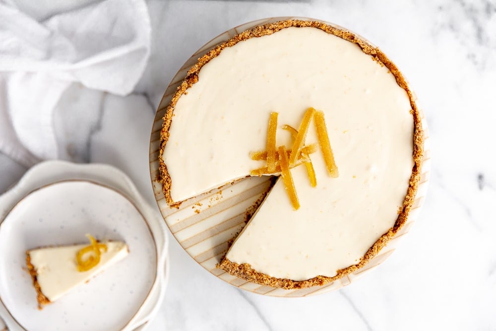 Creamy lemon pie with almond crust on cake stand, with a piece of pie next to it on a plate.