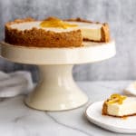 Creamy lemon pie with almond crust on cake stand, with a piece of pie on a plate.