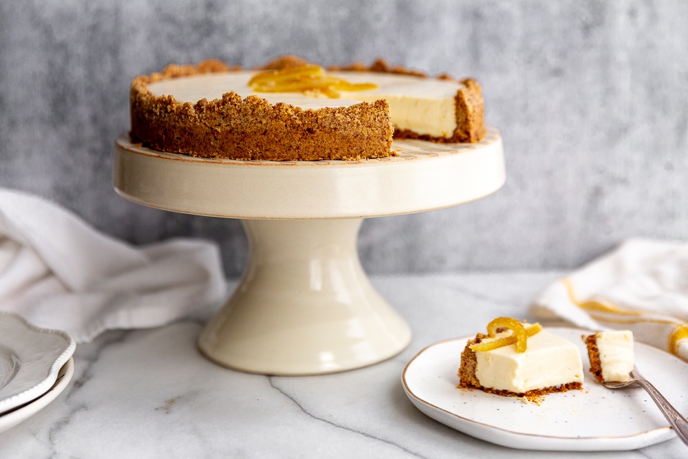 Creamy lemon pie with almond crust on cake stand, with a piece of pie on a plate.