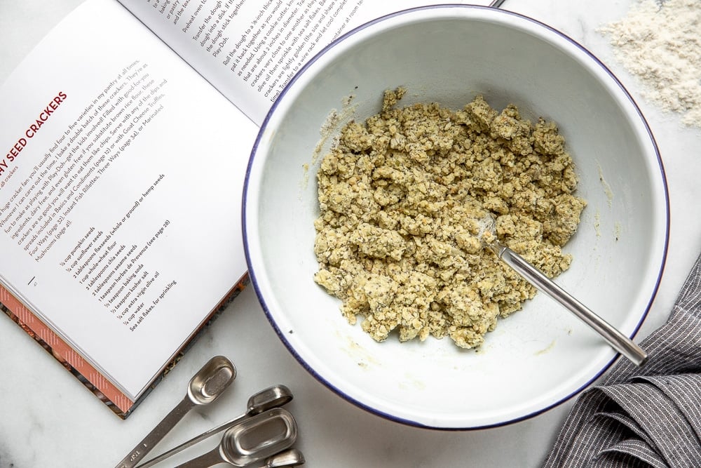 Dough for the seed crackers recipe in a bowl with fork and measuring spoons on the side 