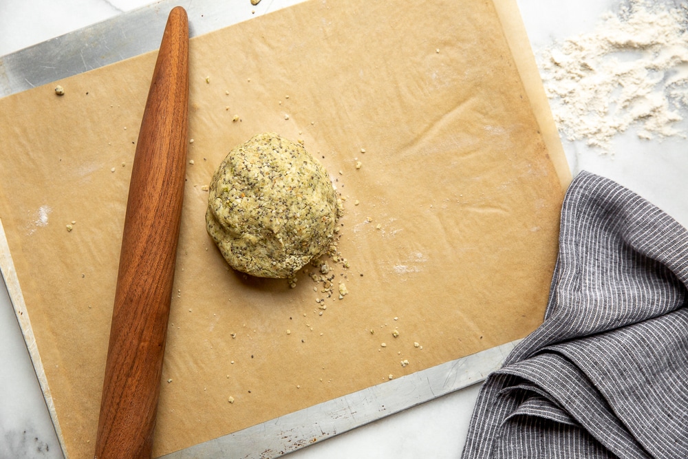 Seed crackers dough in a ball on a piece of parchment paper with a rolling pin