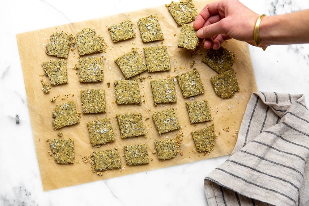 Seed crackers on parchment paper with a hand grabbing a cracker