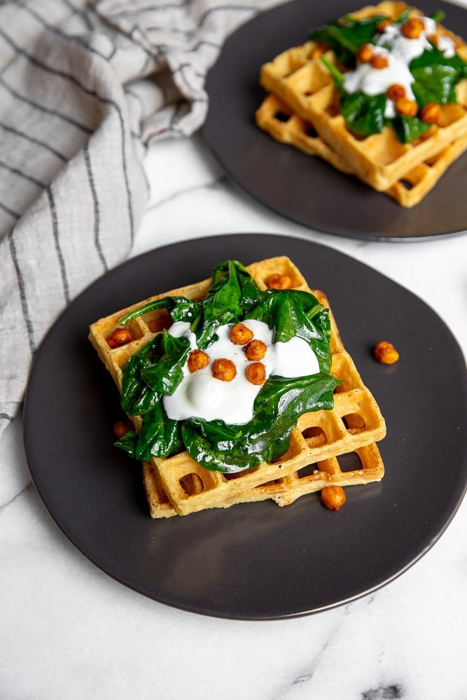 Chickpea waffles on plates, topped with sautéed spinach, yogurt and crispy chickpeas