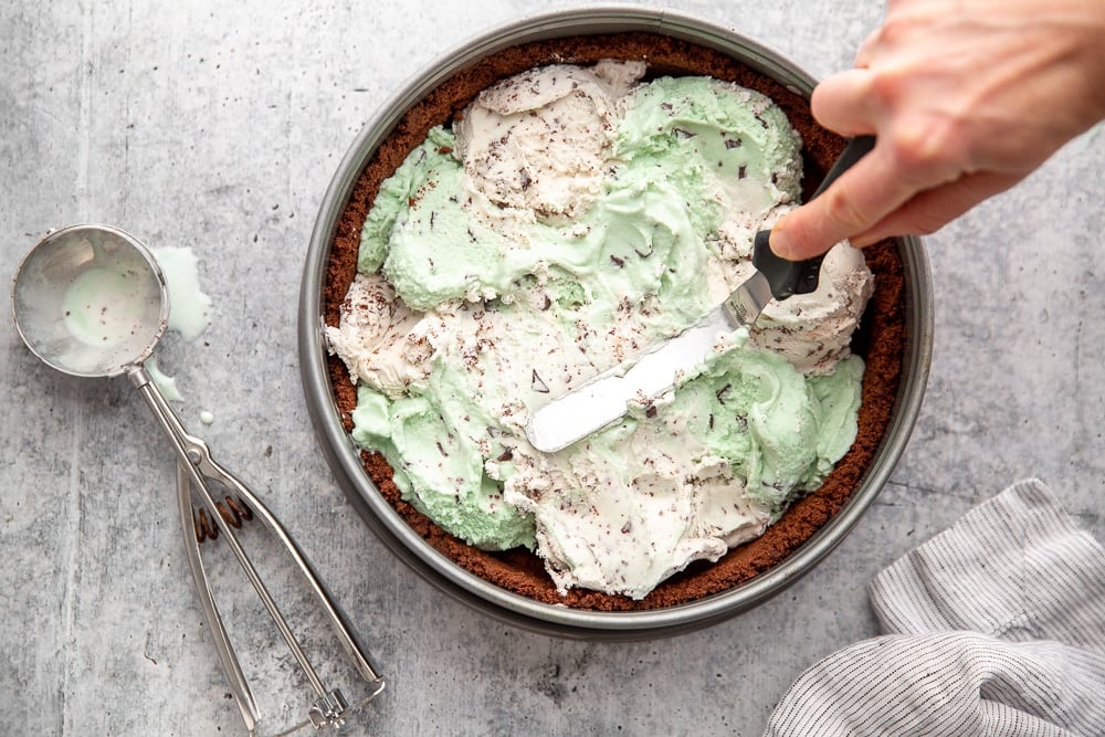 Hand using off-set spatula to spread ice cream in a smooth layer for the ice cream pie 