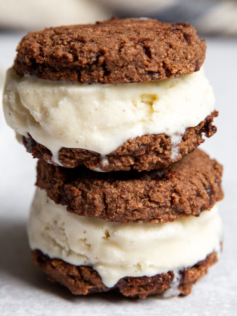 Stack of gluten free ice cream sandwiches with chocolate cookies and vanilla coconut ice cream on a white surface