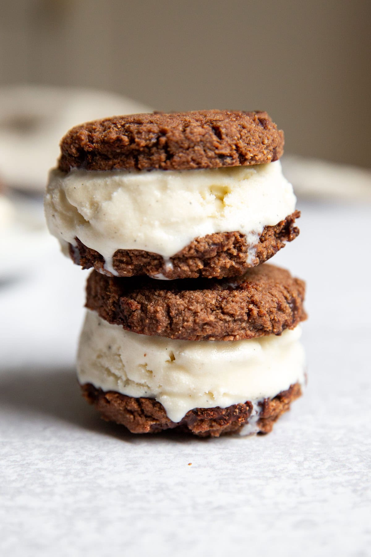 Stack of gluten free ice cream sandwiches with chocolate cookies and vanilla coconut ice cream on a white surface