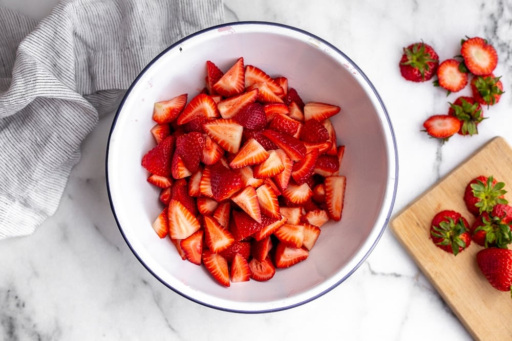 Chopped strawberries in bowl with cutting board on the side