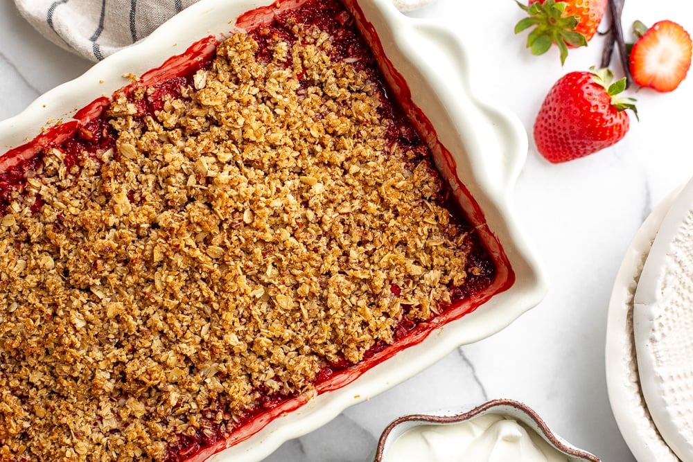 Gluten free strawberry crisp in baking dish with serving bowls alongside