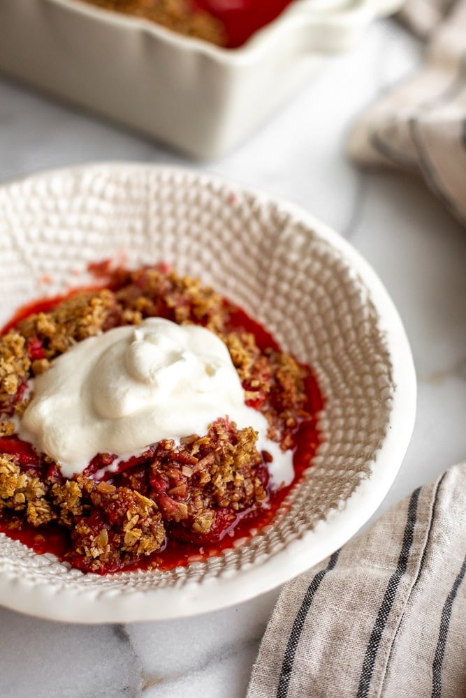 Gluten free strawberry crisp in serving bowl with whipped cream on top