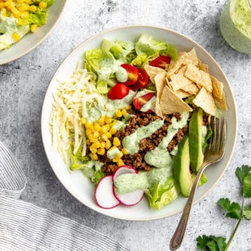 Healthy taco salad in bowl with jar of creamy cilantro lime dressing on the side