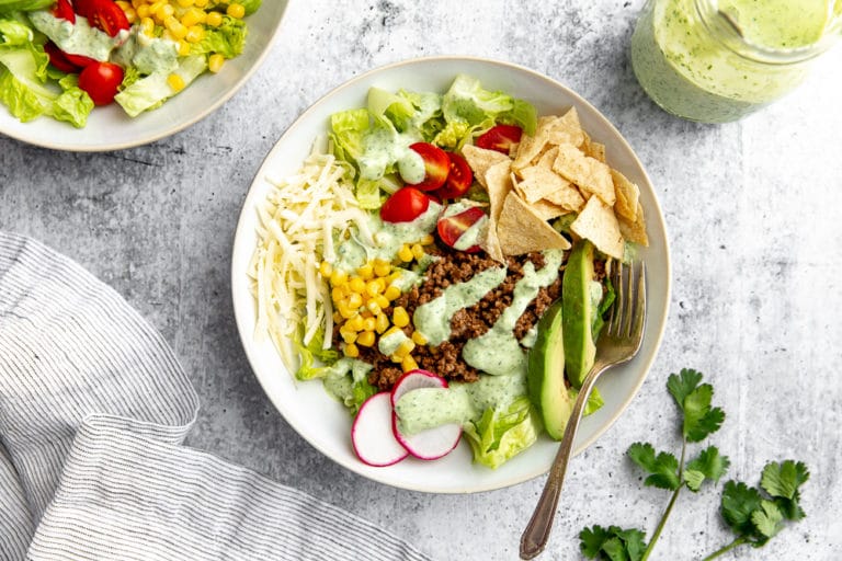 Healthy taco salad in bowl with jar of creamy cilantro lime dressing on the side