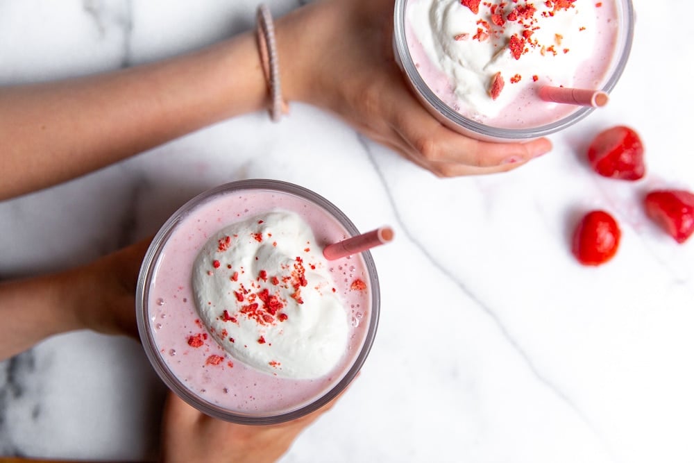 Overhead shot of kids' hands grabbing two strawberry cottage cheese smoothies 