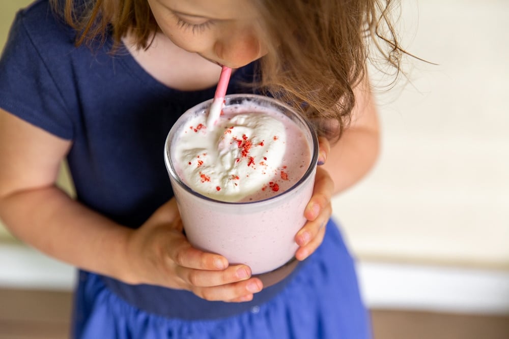 Child drinking strawberry smoothie from a glass with a straw