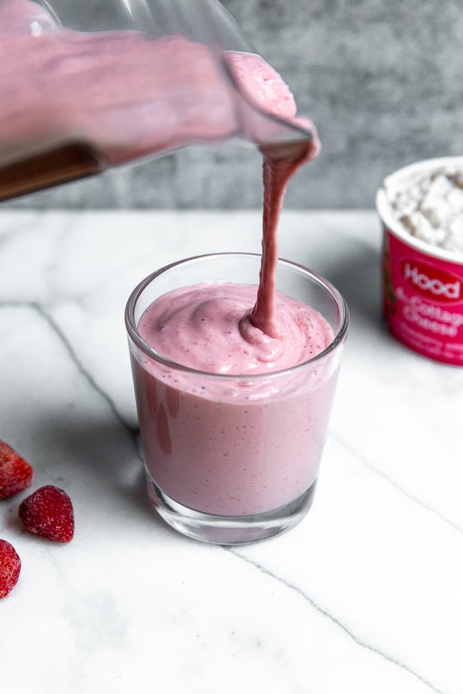 Strawberry smoothie being poured from the blender into a serving glass 