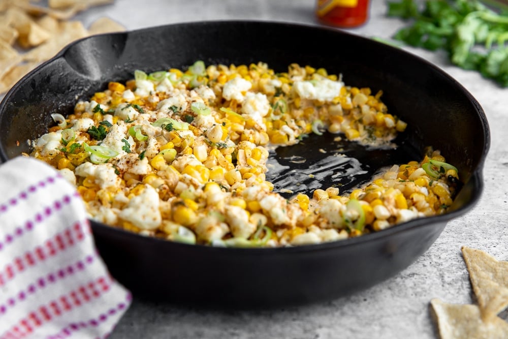 Side angle shot of Mexican street corn dip in cast iron skillet. 