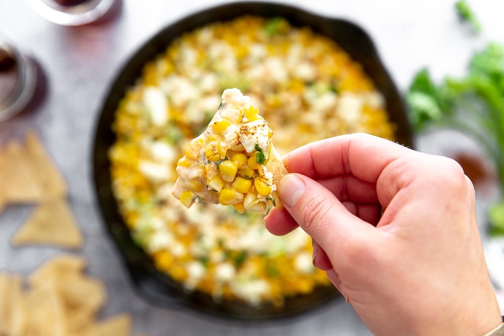 Close up overhead shot of hand holding tortilla chip topped with Mexican street corn dip.