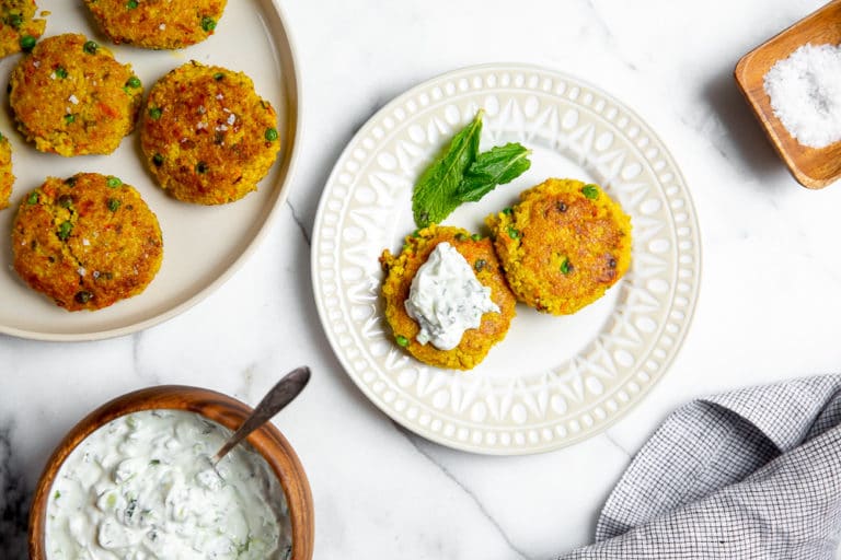 Millet cakes on plate, topped with cucumber mint raita