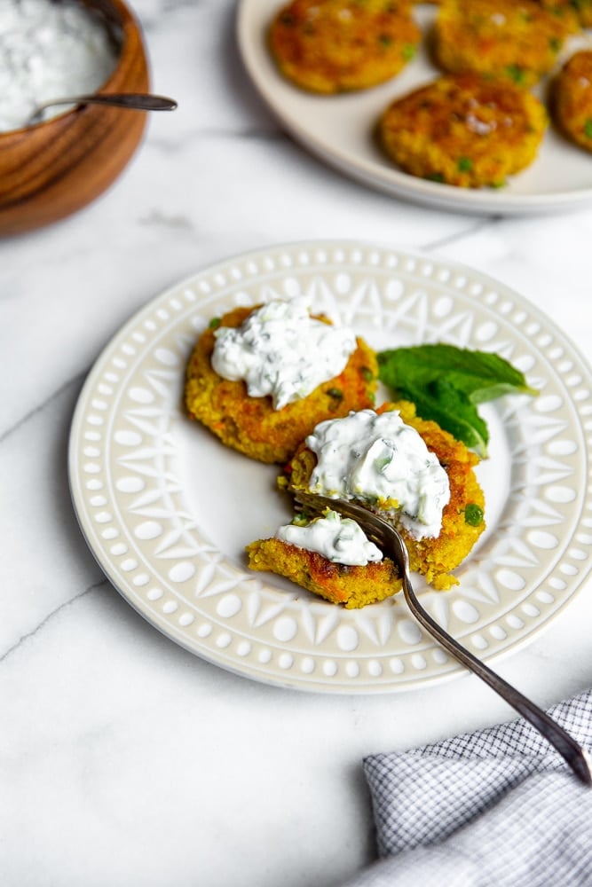 Millet cakes on plate with fork, topped with cucumber mint raita.