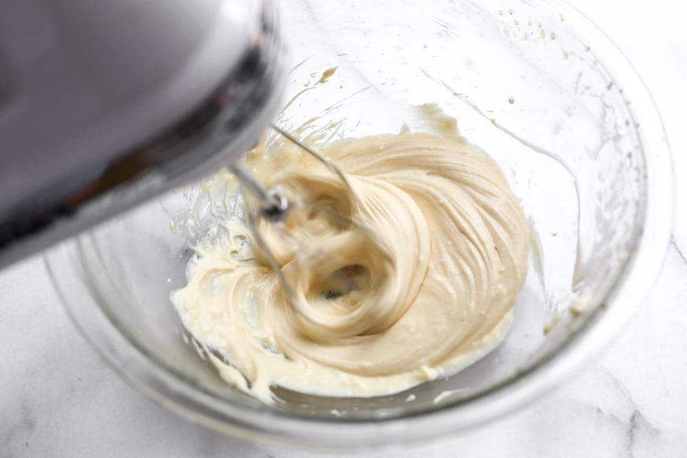 Hand blender mixing the maple cream cheese frosting in a bowl. 