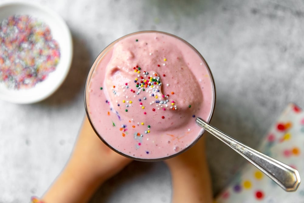 Overhead shot of strawberry frozen yogurt in a glass with sprinkles on top.