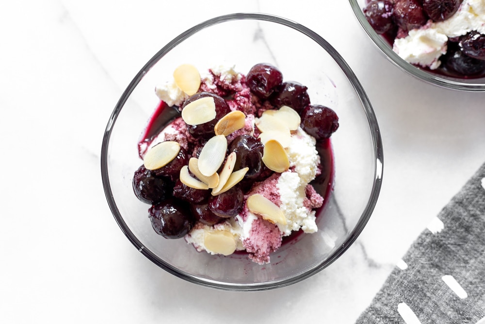 Overhead close up of a bowl of sweet ricotta topped with cherries in port and almonds. 