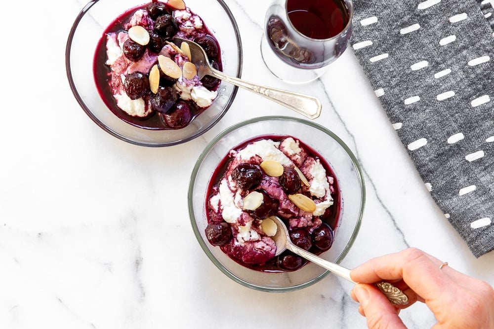 Overhead shot of hand holding a spoon, taking a bite of sweet ricotta with port-braised cherries.