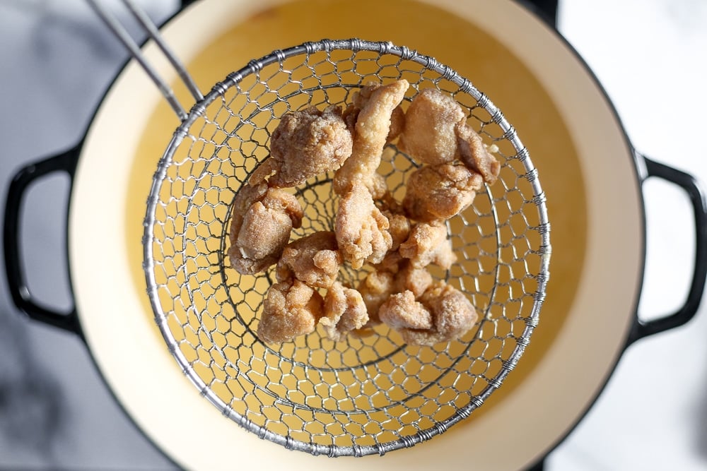 Fried chicken in a strainer coming out of the oil. 