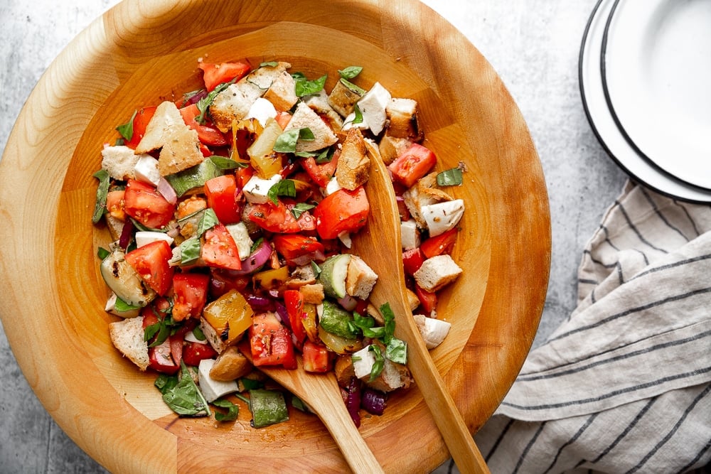 Overhead shot of the grilled panzanella salad in a large wooden salad bowl, with serving bowls alongside.