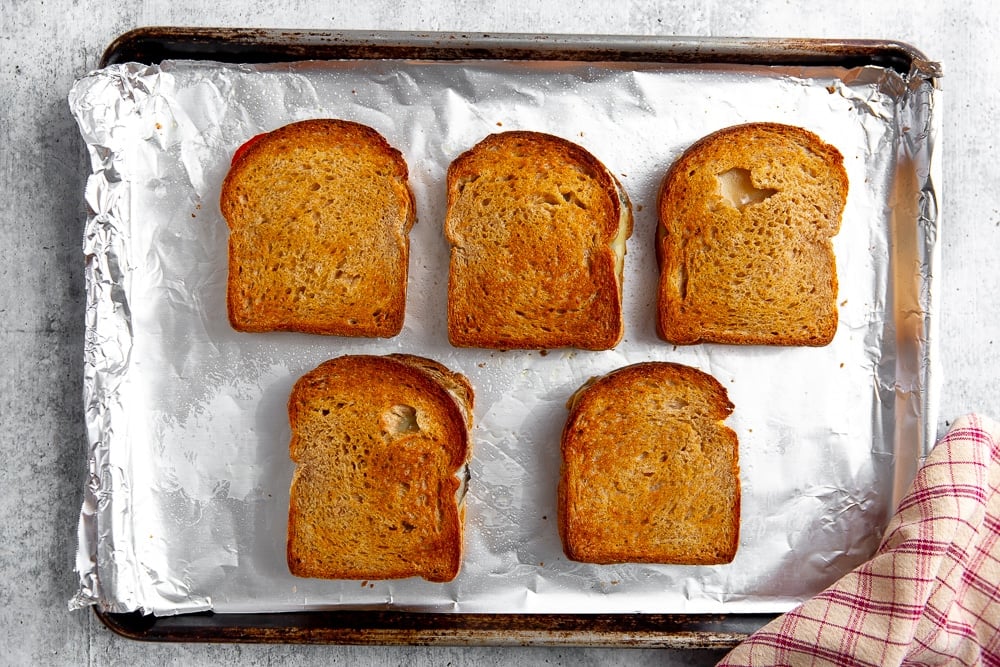 Overhead shot of five grilled cheese sandwiches lined up on a sheet pan.