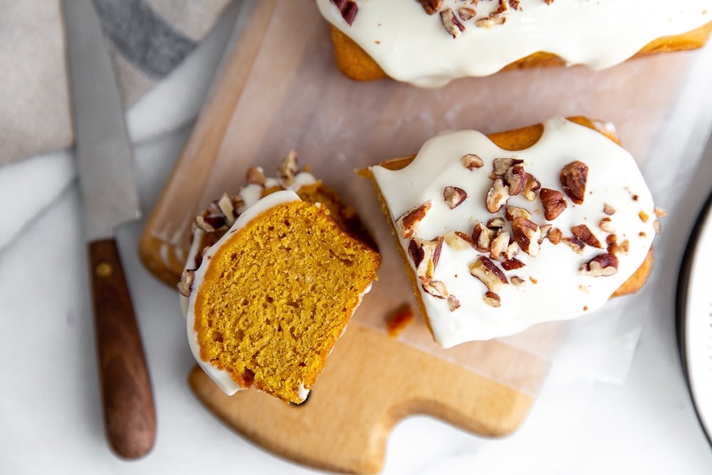 Overhead shot of a slice of pumpkin cake on a wooden serving board with a knife alongside.