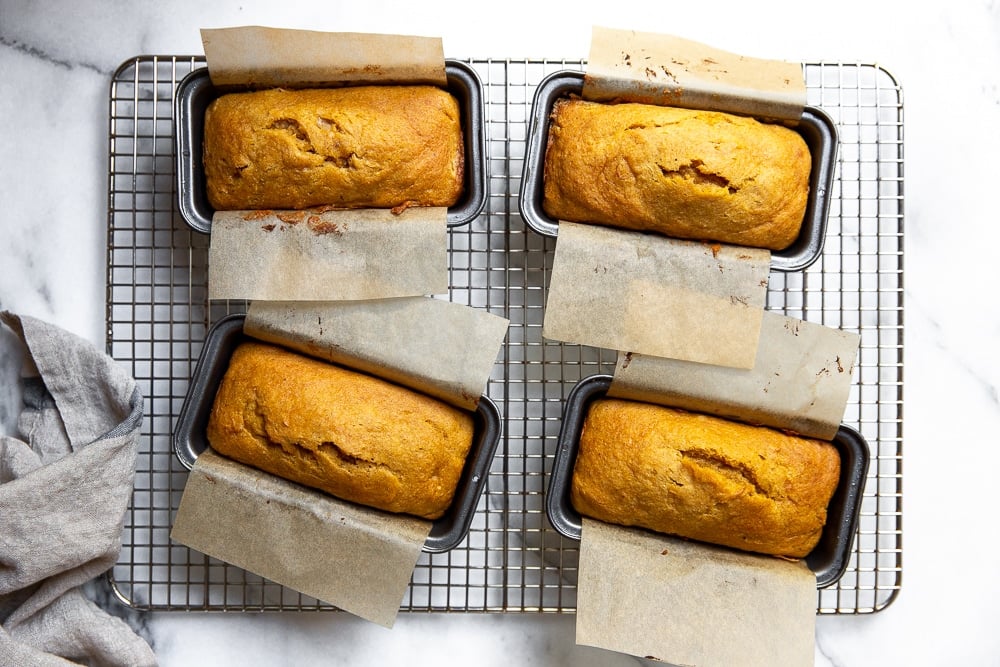 Four mini pumpkin pound cakes in baking pans on a cooling rack.