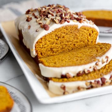 Sliced pumpkin pound cake on a platter with plates to the side.