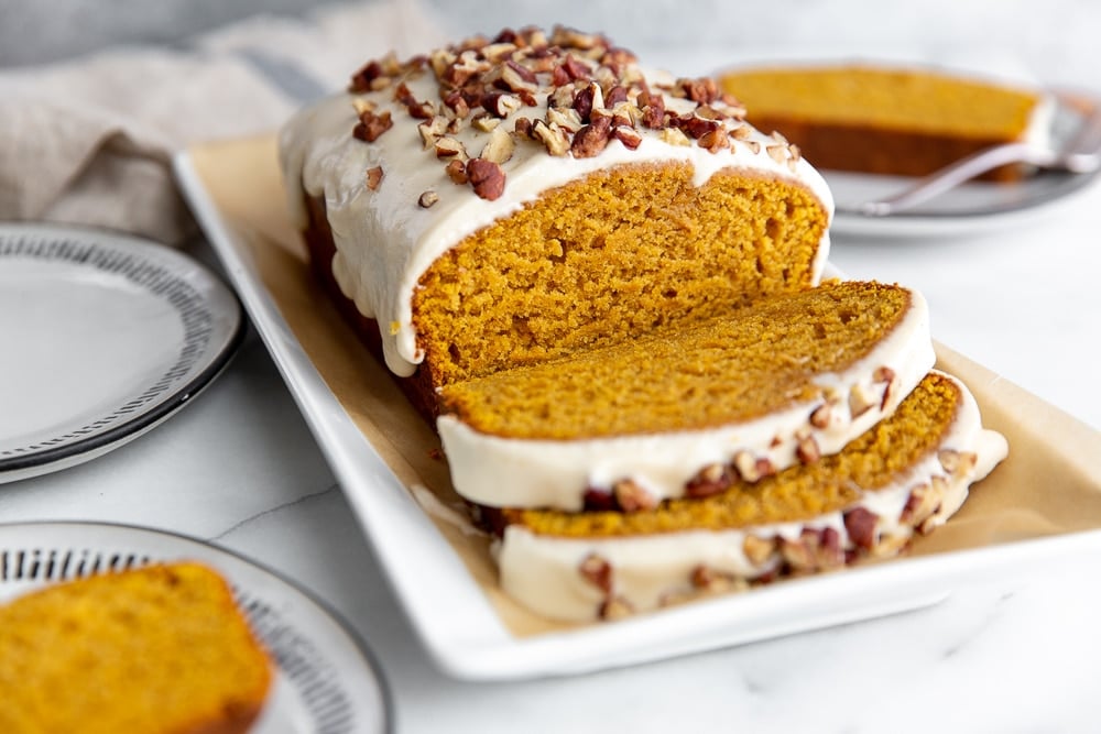 Sliced pumpkin pound cake on a platter with plates to the side.