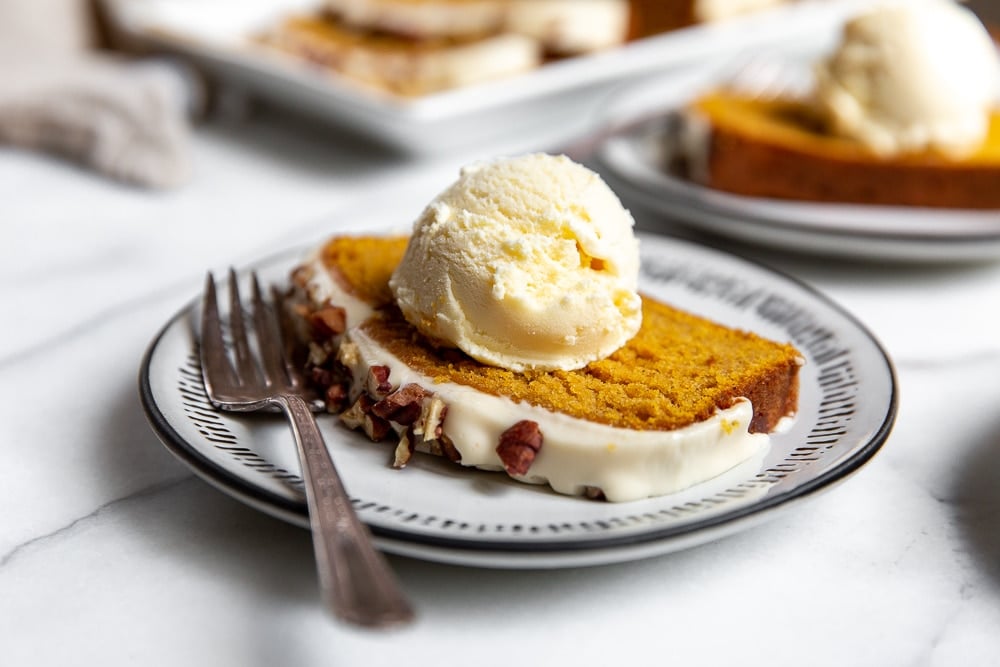 A slice of gluten free pumpkin pound cake on a plate topped with a scoop of ice cream.  