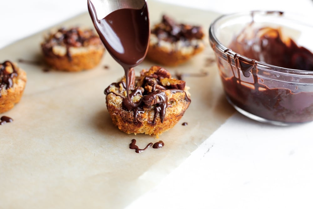 Spoon drizzling chocolate over a gluten free pecan tart.