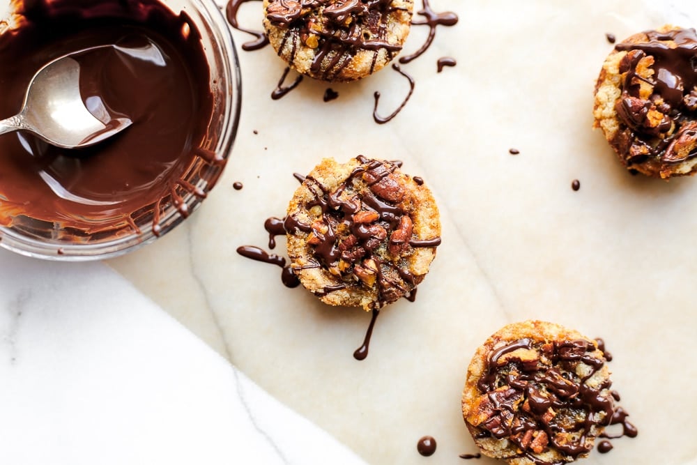 Mini gluten free pecan Christmas tarts on a piece of parchment paper, drizzled with chocolate. 