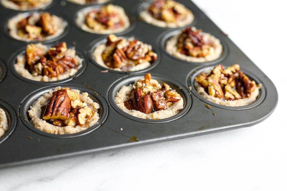 Close up of unbaked pecan tarts in the muffin tin. 